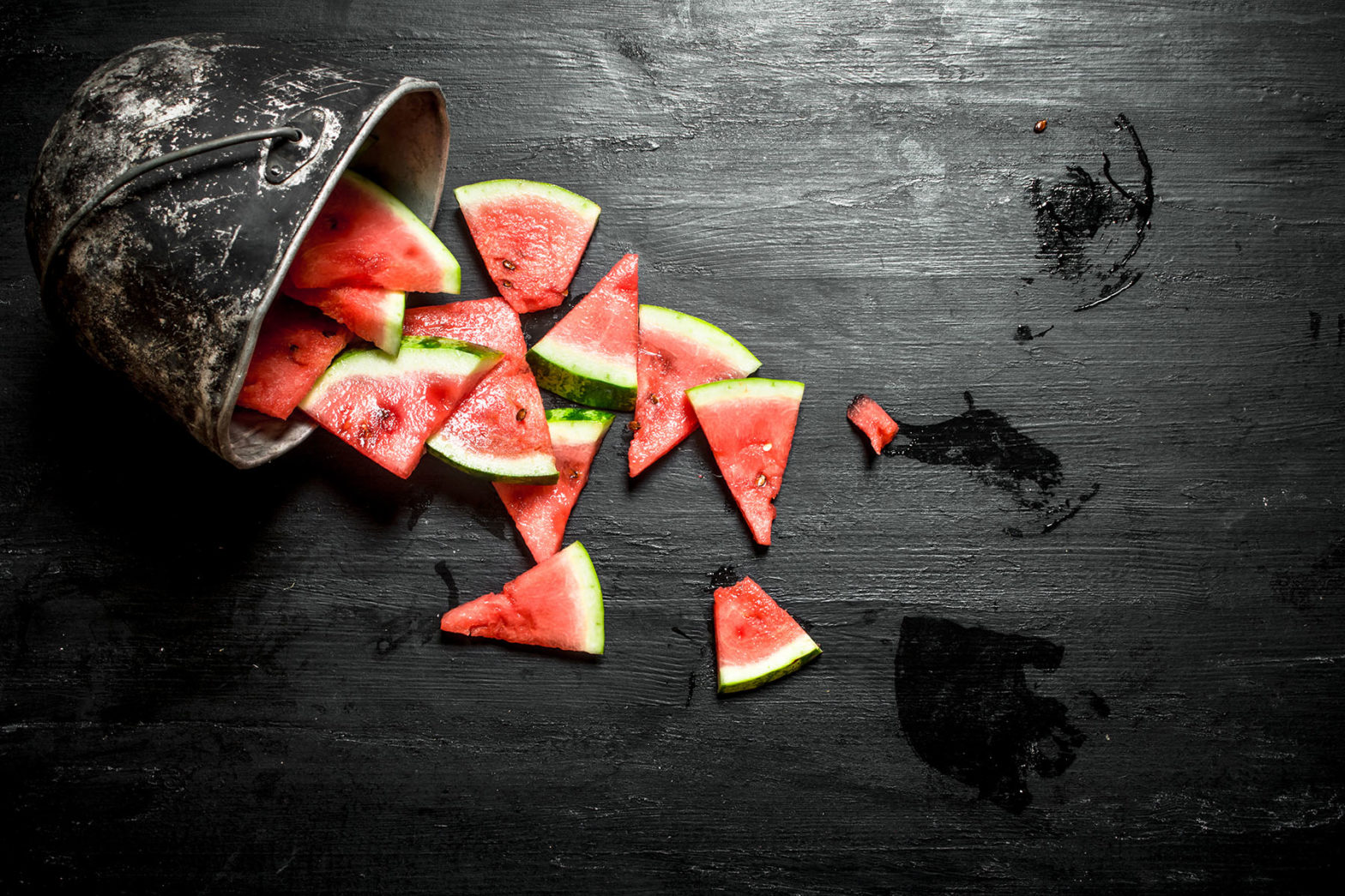 Chopped pieces of watermelon in an old pot. On the black wooden table.